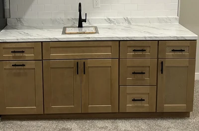 Wood cabinet fronts, dark pulls, a pale veined counter and white tile backsplash.