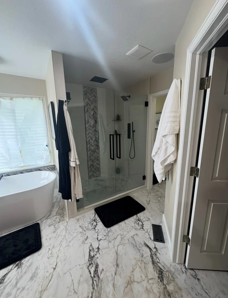 Freestanding tub beside a glass-enclosed shower with a mosaic tile accent and marble-look floor tile.