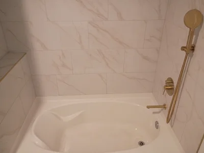 Brass-tone bath fixtures beside veined wall tile and a white tub.