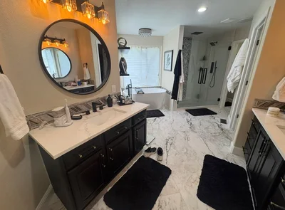 Dark double vanities leading to a freestanding tub and glass shower.