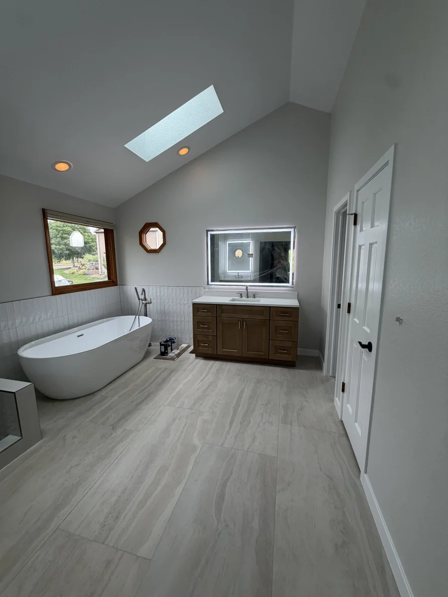 Skylit bathroom with large-format floor tile, a freestanding tub and a wood vanity.