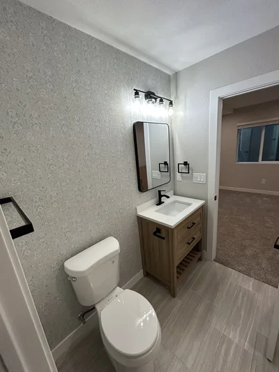 Wood vanity and black-framed mirror beside a patterned bathroom wall.
