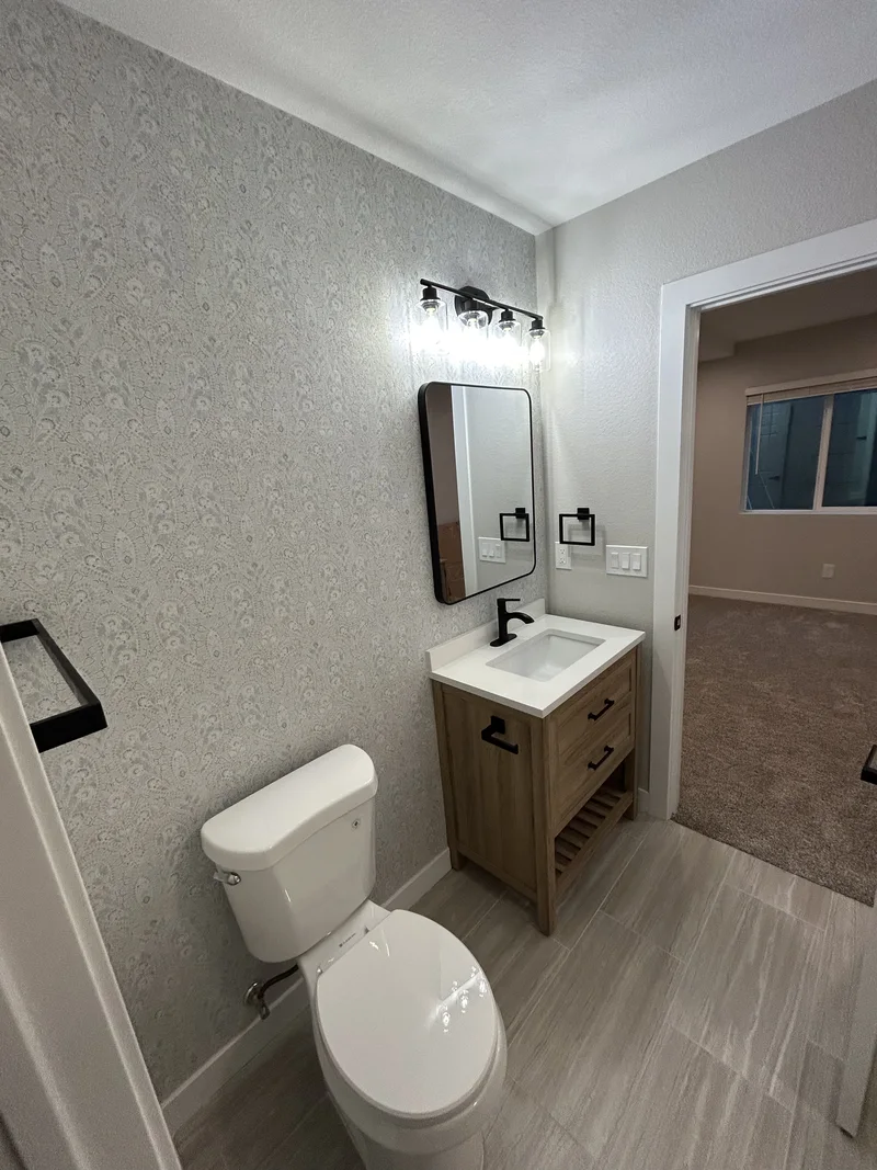 Bathroom with a wood vanity, black-framed mirror and a patterned wall.