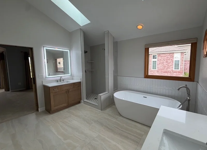 Remodeled bathroom with skylights, a freestanding tub, wood vanity and walk-in shower, by Interiors of Idaho.