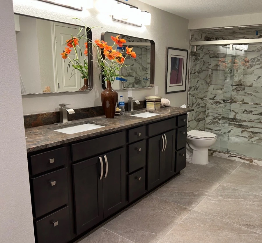 Dark double vanity with a stone-look counter beside a glass shower with marble-look wall tile.